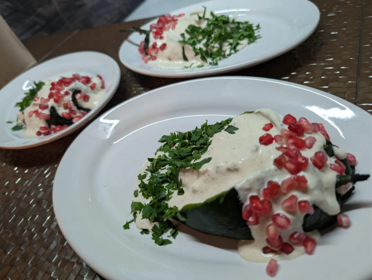 Tres chiles en nogada servidos con nogada, granada y hierbas frescas.